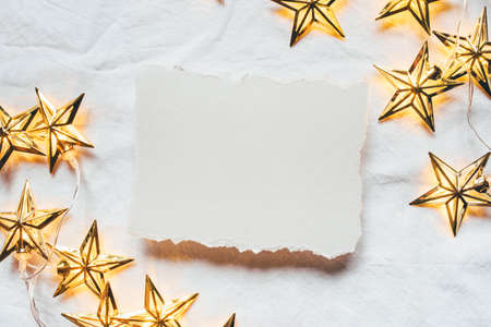 Greeting card for Christmas or New year of golden garlands in the shape of stars with a paper card-note. Flat lay. Minimal concept.の写真素材