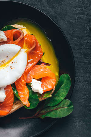 Sandwich with salmon, cheese, herbs and poached egg on black background. Top view.