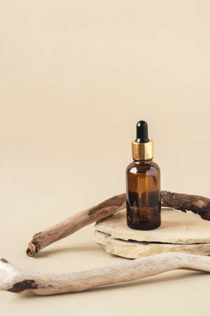 One brown cosmetic bottle on a natural beige background. A stone podium and a driftwood. Front view.の写真素材
