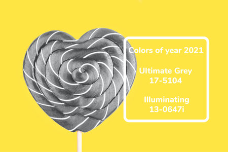 Gray lollipop in the shape of a heart on a yellow background. Flat lay, top view. Colors 2021.の写真素材