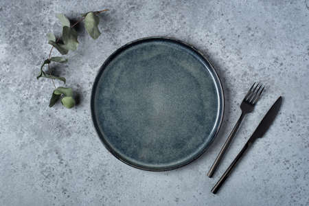 An empty plate and cutlery on a gray table. Top view.