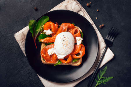 Sandwich with salmon, cheese, herbs and poached egg on black background. Top view.の写真素材