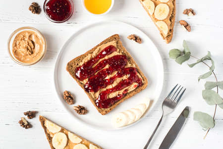 Homemade peanut butter sandwiches with raspberry jam and banana on white wooden background. Top...