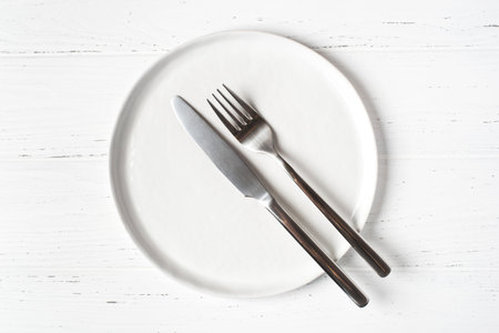 An empty plate and cutlery on a white wooden table. Top view.の写真素材