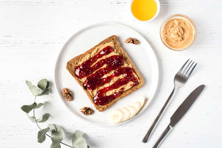 Homemade peanut butter sandwiches with raspberry jam and banana on white wooden background. Top view.の写真素材