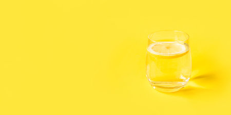 Glass of water with lemon on a yellow background. Summer refreshing drink.の写真素材