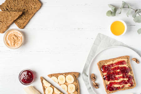 Homemade peanut butter sandwiches with raspberry jam and banana on white wooden background. Top...