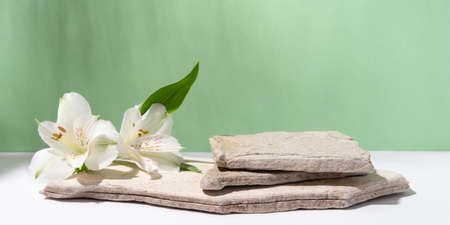 Background for cosmetic products of natural green color. Stone podium with white flowers. Front view.の写真素材