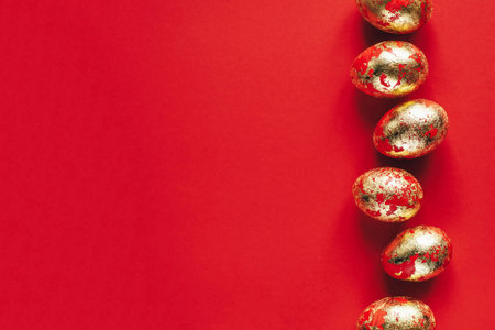 Golden colored and decorated with sparkles Easter eggs on red background.の写真素材