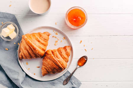Plate with two fresh croissants, jam and coffee on white wooden table.の写真素材