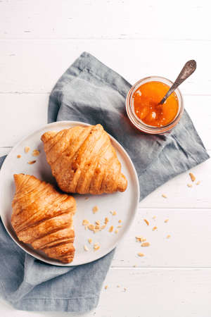 Plate with two fresh croissants and jam on white wooden table.の写真素材