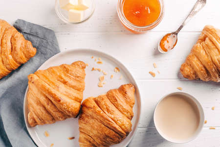 Plate with two fresh croissants, jam and coffee on white wooden table.の写真素材