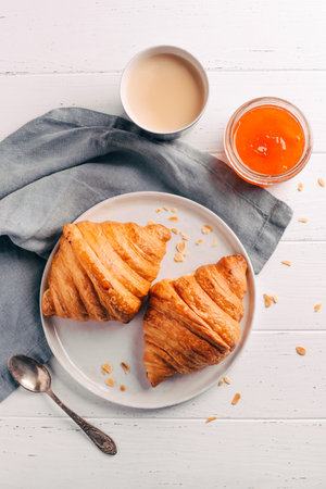 Plate with two fresh croissants, jam and coffee on white wooden table.の写真素材