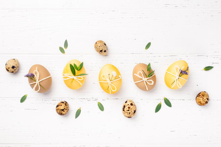 Festive Easter background. Yellow and brown Easter eggs with flowers on a white wooden table. top view.の写真素材
