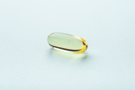 One omega 3 fish liver oil capsule on blue background. Close up, front view.の写真素材