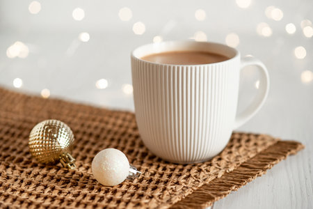 A white cup with hot coffee or tea on a white wooden table with Christmas lights.の写真素材
