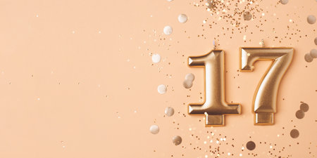 Gold candles in the form of number seventeen on peach background with confetti. 17 years celebration.の写真素材