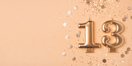 Gold candles in the form of number thirteen on peach background with confetti. 13 years celebration.の写真素材