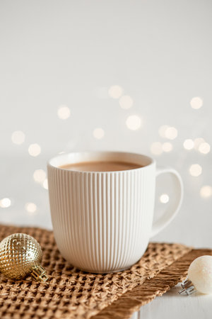 A white cup with hot coffee or tea on a white wooden table with Christmas lights.の写真素材