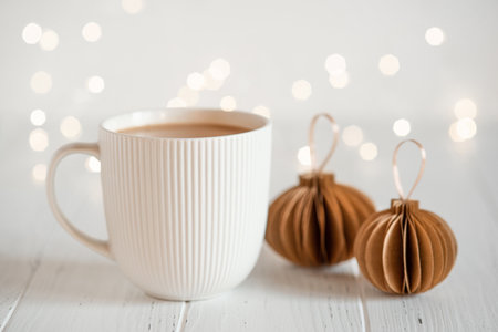 A white cup with hot coffee or tea on a white wooden table with Christmas lights.の写真素材