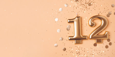 Gold candles in the form of number twelve on peach background with confetti. 12 years celebration.の写真素材