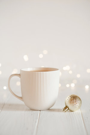 A white cup with hot coffee or tea on a white wooden table with Christmas lights.の写真素材