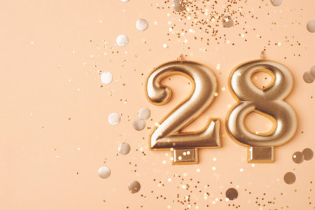 28 years celebration. Greeting banner. Gold candles in the form of number twenty eight on peach background with confetti.の写真素材