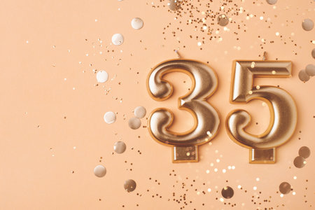 35 years celebration. Greeting banner. Gold candles in the form of number five thirty on peach background with confetti.の写真素材