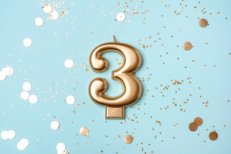 Gold candle in the form of number three on blue background with confetti.の写真素材