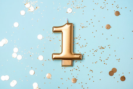 Gold candle in the form of number one on blue background with confetti.の写真素材