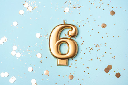 Gold candle in the form of number six on blue background with confetti.の写真素材
