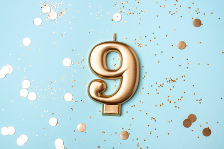Gold candle in the form of number nine on blue background with confetti.の写真素材