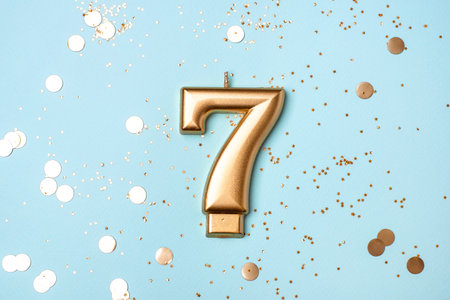 Gold candle in the form of number seven on blue background with confetti.