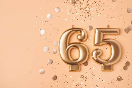 65 years celebration. Greeting banner. Gold candles in the form of number sixty five on peach background with confetti.の写真素材