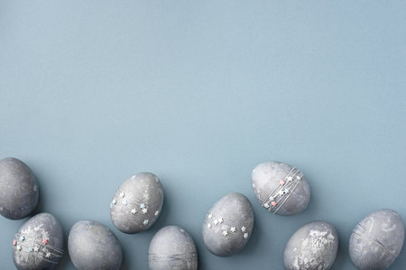 Festive Easter background. Gray-blue Easter eggs with stars on a blue table. Card with a place for text. Top view.の写真素材