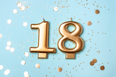 Gold candles in the form of number eighteen on blue background with confetti. 18 years celebration. Greeting banner.の写真素材