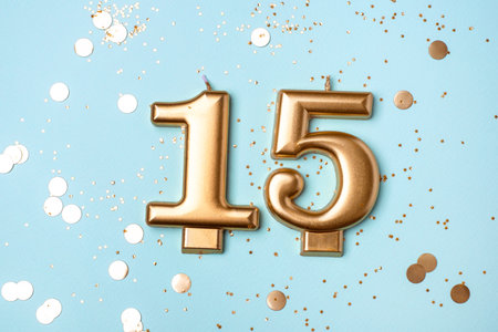 Gold candles in the form of number fifteen on blue background with confetti. 15 years celebration.の写真素材