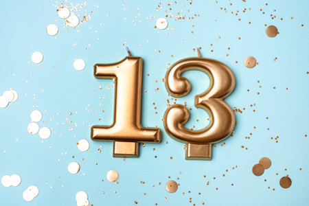 Gold candles in the form of number thirteen on blue background with confetti. 13 years celebration.の写真素材