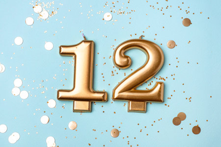 Gold candles in the form of number twelve on blue background with confetti. 12 years celebration.の写真素材