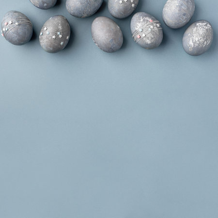 Festive Easter background. Gray-blue Easter eggs with stars on a blue table. Banner with a place for text. Top view.の写真素材