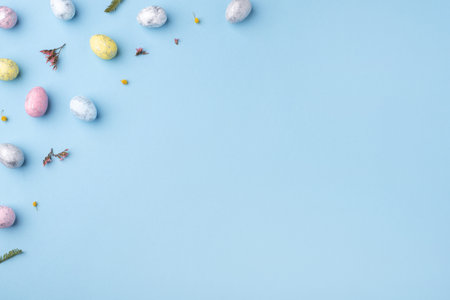 Festive Easter background. Multicolored Easter eggs and flowers on a blue table. Card with a place for text. Top view.の写真素材