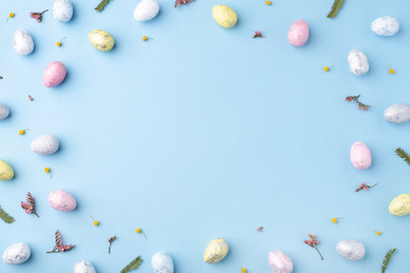 Festive Easter background. Multicolored Easter eggs and flowers on a blue table. Card with a place for text. Top view.の写真素材