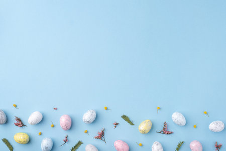Festive Easter background. Multicolored Easter eggs and flowers on a blue table. Card with a place for text. Top view.の写真素材