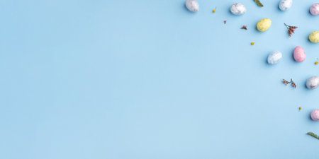 Festive Easter background. Multicolored Easter eggs and flowers on a blue table. Banner with a place for text. Top view.の写真素材