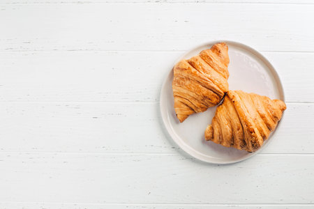 Plate with two fresh croissants on white wooden table. Top view.の写真素材