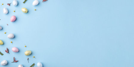 Festive Easter background. Multicolored Easter eggs and flowers on a blue table. Banner with a place for text. Top view.の写真素材