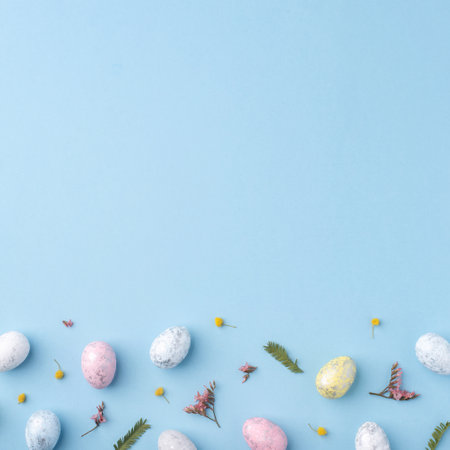 Festive Easter background. Multicolored Easter eggs and flowers on a blue table. Card with a place for text. Top view.の写真素材