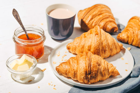 Plate with fresh croissants, jam and coffee on white wooden table.の写真素材