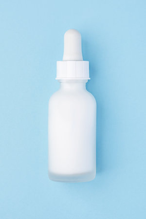 A frosted white dropper bottle with a minimalist design on a pastel blue background. Perfect for...