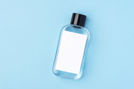 A cosmetic glass bottle with a blank white label on a pastel blue background. Perfect for showcasing...